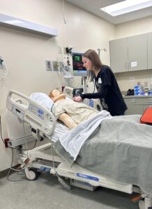 A high school students practices nursing skills on a dummy at a lab.